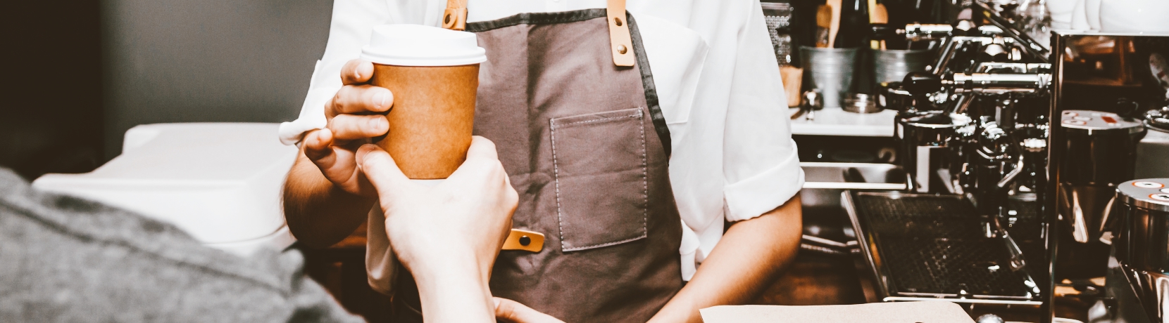 An image of a barista handing a cup of coffee to a customer.