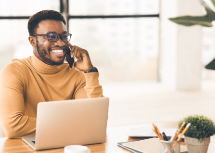 Photo of a young man talking on the phone in front of his laptop