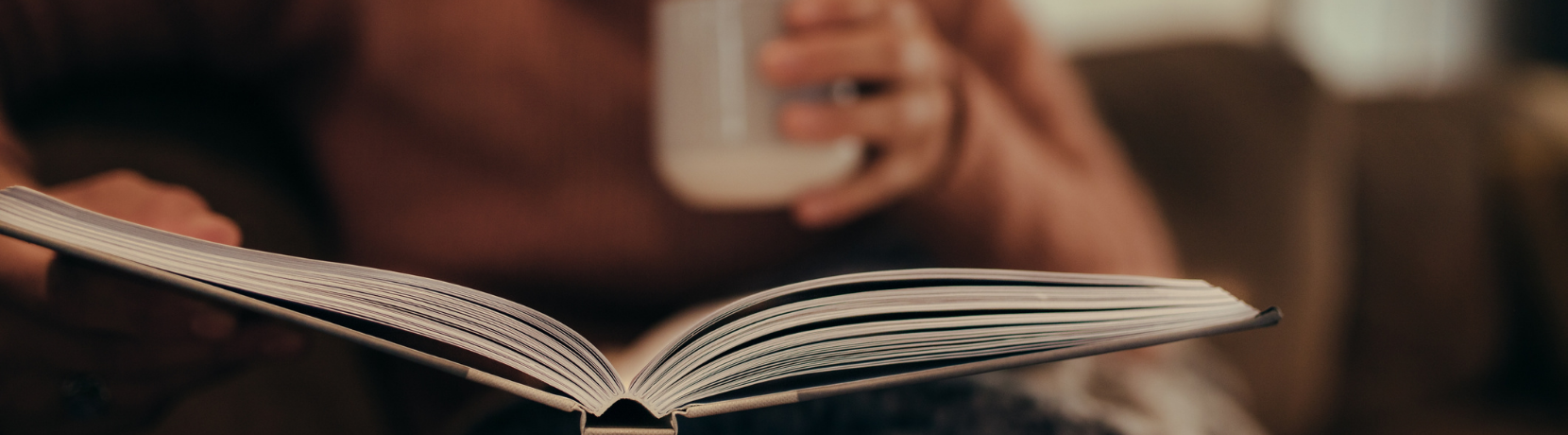 Photo of woman holding a coffee and reading a book