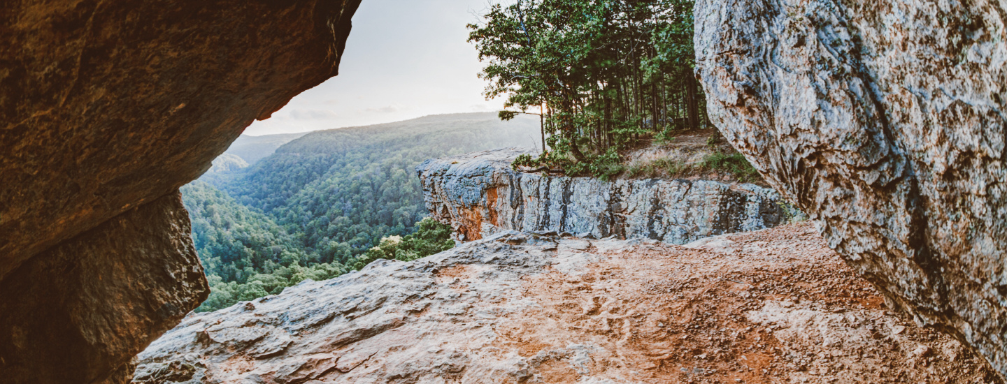 Shot looking out of the entrance of a cave overlooking lush green hills