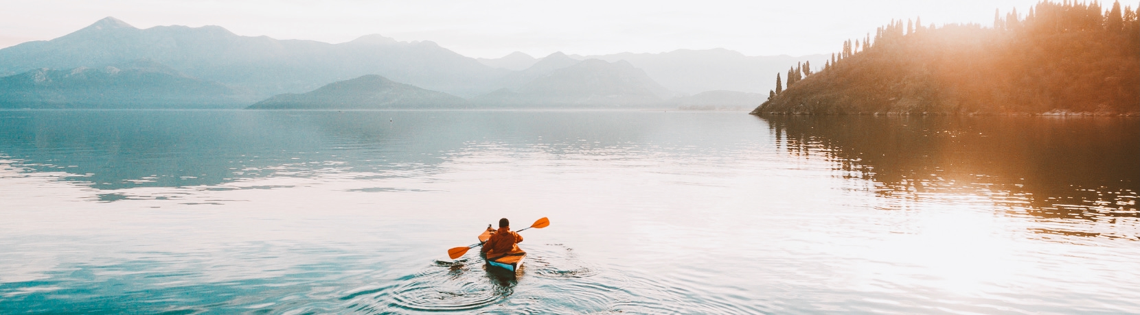 A landscape picture of a lake with someone in a kayak.